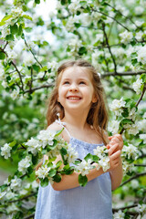 A happy girl is playing under a blooming apple tree with white flowers. A child holds a white flower in his hands.. Summer fun for families with children outdoors in the beautiful spring garden.