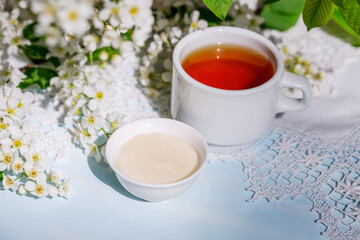 Spring still life with bird cherry flowers, herbal tea and honey cream. Horizontal photo in vintage style.