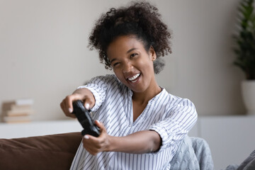 Happy positive millennial african ethnic multiracial woman holding remote controller in hands,...