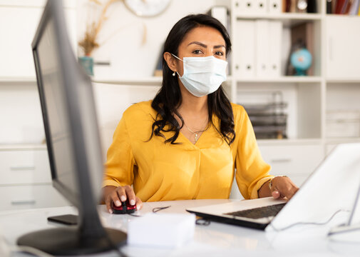 Focused Hispanic Businesswoman In Disposable Face Mask Working On Computer In Office. Necessary Precautions During COVID 19 Pandemic.