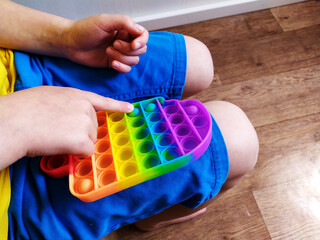 Boy in blue shorts play with colorful poppit fidget toy. Anti-stress sensory toy on white background