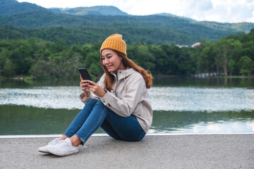 A young asian woman holding and using mobile phone while traveling mountains and lake