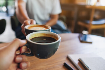 Closeup image of a man and a woman clinking white coffee mugs in cafe