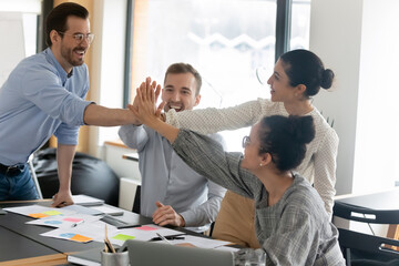 Excited diverse colleagues giving high five at meeting, celebrating shared success, great teamwork results, overjoyed employees team coworkers involved in team building activity at briefing