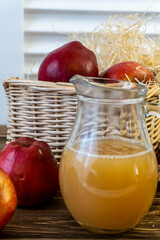 Red apples in a basket and apple juice in a jug on a wooden table
