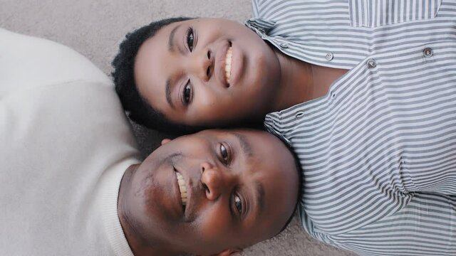 Top view African couple of married man and woman lying on floor indoors of new home looking at camera. Shooting from above ethnic black afro faces heads wife and husband people in love smiling toothy