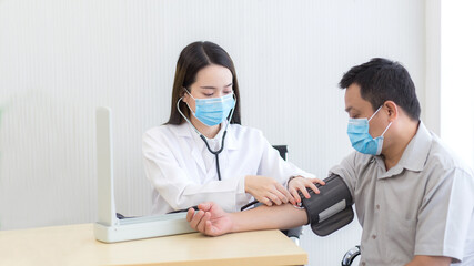 Asian female doctor measure blood pressure of a man patient by using a blood pressure meter at hospital while they wear a medical face mask to anti infection of respiratory system.