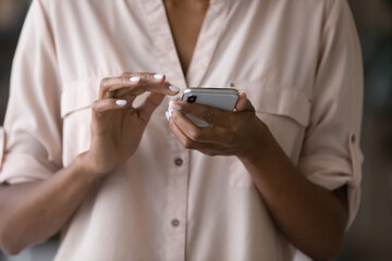 Close up millennial african woman holding phone in hands, typing message involved in distant communication in social network, web surfing information online or playing video game, addiction concept.
