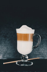 Cafe latte macchiato layered coffee in a glass coffee glass. Coffee cup with foam  and a straw for drinks