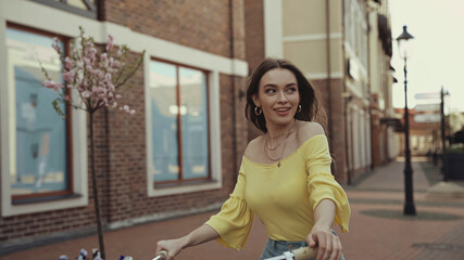 happy young woman in yellow blouse looking away while riding on bicycle outside.