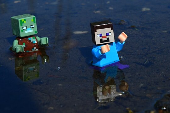 Minecraft LEGO Figure Of Drowned Zombie Mob Chasing Scared Figure Of Steve In Shallow Waters, Daylight Sunshine.