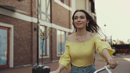 Fototapeta premium joyful young woman in yellow blouse smiling while riding on bicycle outside.