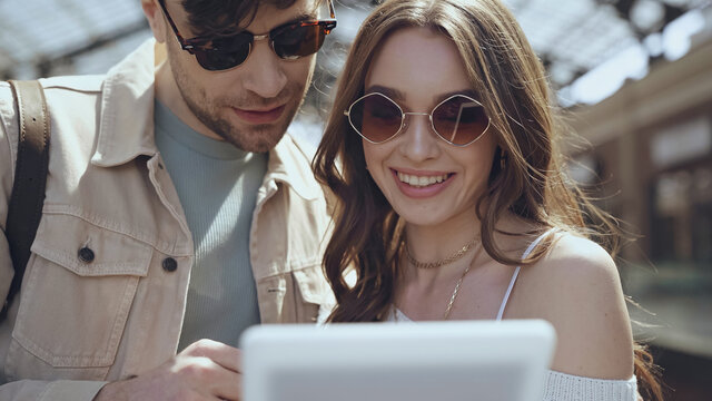 happy man and woman in sunglasses using blurred digital tablet.
