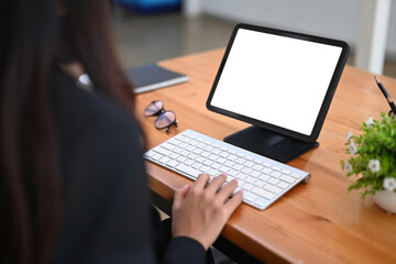 Fototapeta na wymiar Rear view of businesswoman typing on wireless keyboard while working with digital tablet.