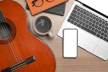 Above view of laptop, smart phone and classical guitar on wooden floor.