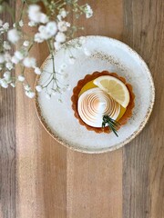Top view lemon cheese tart on white ceramic plate on wooden table in coffee cafe. white flowers foreground.