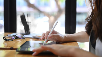 Close up view of businesswoman holding stylus pen writing on digital tablet while sitting near...