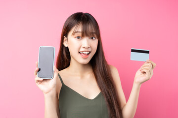 Fototapeta premium Beautiful young asian girl using phone on pink background