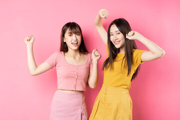 Portrait of two beautiful young Asian girls posing on pink background