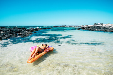 Fototapeta na wymiar Beautiful beach and tropical ocean water with pretty woman lay down on a colorful inflatable mattress lilo relaxing and enjoying the sea nature and the beach in summer holiday vacation