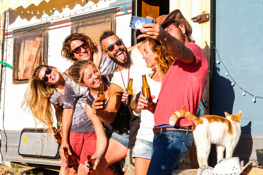 Group of young people friends take selfie picture in country side vacation lifestyle and old caravan camper in background - alternative millenial lifestyle men and women