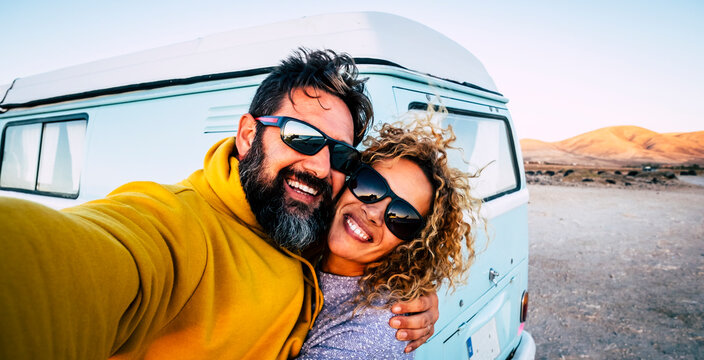 Happy adult couple smile and have fun together taking selfie picture with old vintage classic van in background - concept of vanlife and travel people - changing life man and woman