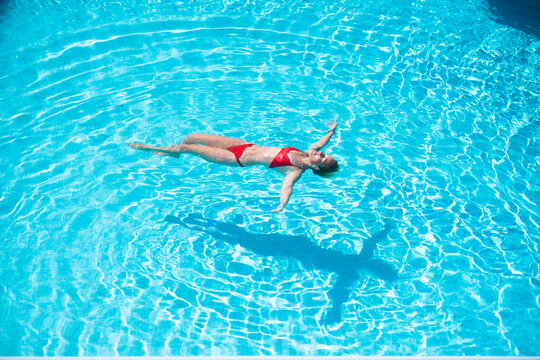 Young caucasian woman relax and enjoy summer holiday vacation floating laying on the water at the pool in hotel residence - happy adult people and tropical luxury lifestyle - red bikini