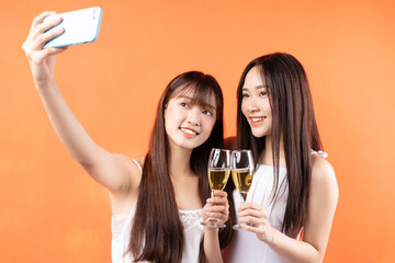 Two beautiful young Asian girls raising wine glasses on orange background
