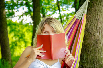 happy girl reading a book in a hammock outdoors in the park