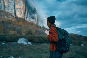 woman traveler in a sweater with a backpack on her back in autumn in the mountains on nature and sky clouds