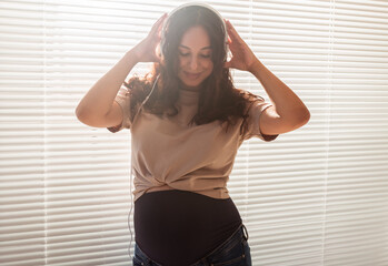 Smiling brunette pacified pregnant woman listening to pleasant music using a smartphone and headphones. Sedation therapy concept before meeting with baby