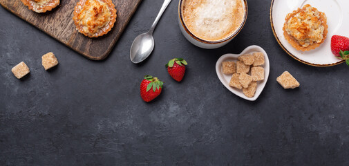 Cup of coffee, cakes and strawberries on a wooden cutting board on dark stone background. Horizontal banner. Top view