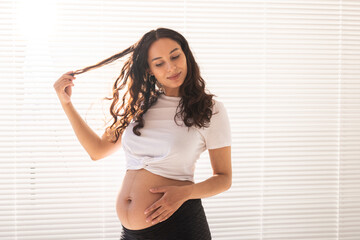 Smiling young beautiful pregnant woman touching her belly and hair and rejoicing. Concept of health and thinking about the future while waiting for baby. Copyspace