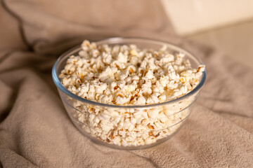 Bowl of popcorn for watching a film on a beige couch. Snacks and unhealthy junk food concept