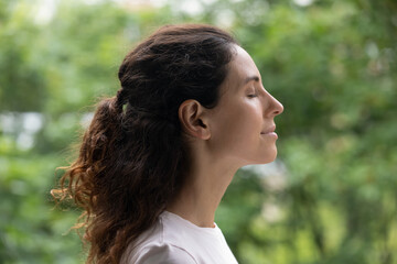 Head shot side view peaceful happy young hispanic woman standing with closed eyes, breathing fresh...