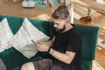 Relaxed man using a smartphone sitting on green couch in the living room at home