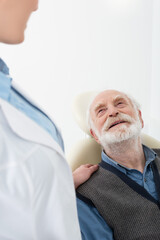 smiling senior patient lying in dental chair with dentist hand on shoulder.
