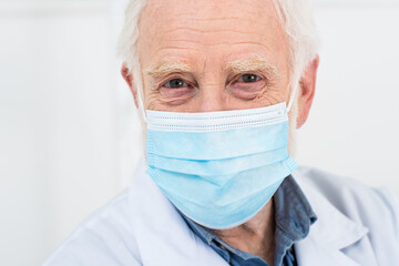 Fototapeta premium portrait of senior doctor in white coat and medical mask on grey background.