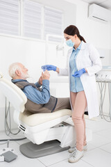 Obraz premium caring dentist giving glass of water to senior patient lying in dental chair.
