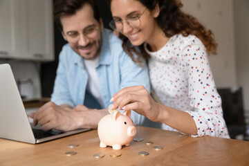 Happy millennial family couple putting coins in piggybank, planning vacation or investments...