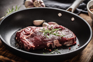 Fresh raw beef Ribe Eye steak in teflon pan with rosemary, garlic, salt and pepper