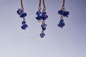 Cropped shot of asymmetrical handmade earrings with purple beads isolated over light purple...
