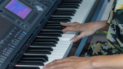 Young female student in casual black attire enjoys playing piano at a hotel lobby. Pianist has a happy time with his electric musical instrument.