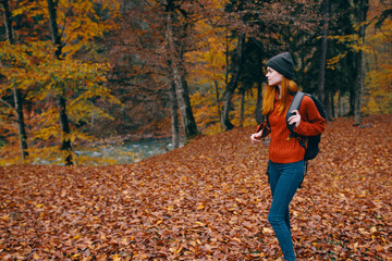 woman in a hat in a red sweater and jeans walks in the park with a backpack on her back travel tourism autumn landscape