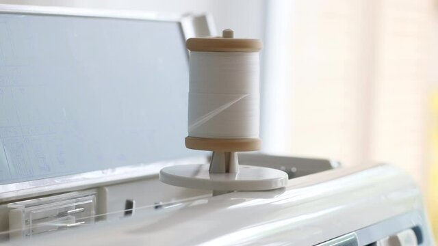 Close up of a spool with white thin thread on working a new sewing machine. Spool with thin white thread on working a sewing machine.