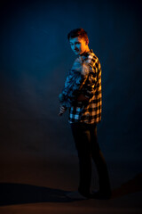 A guy in a plaid shirt with a dust brush on a dark background illuminated by blue and yellow light