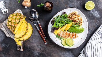Healthy dinner. Buddha bowl lunch with grilled chicken breast, halloumi, pineapple, avocado, green rocket salad, lime and olive oil. on gray background. Flat lay. Top view