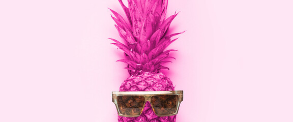 pink whole pineapple in sunglasses on a pink background. Top view, flat lay. Banner