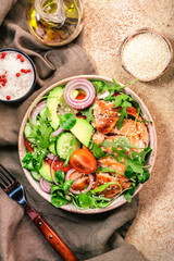 Grilled chicken salad with tomatoes, arugula, red onion, avocado, sesame seeds and lemon oil dressing. Healthy food. Beige background. Top view