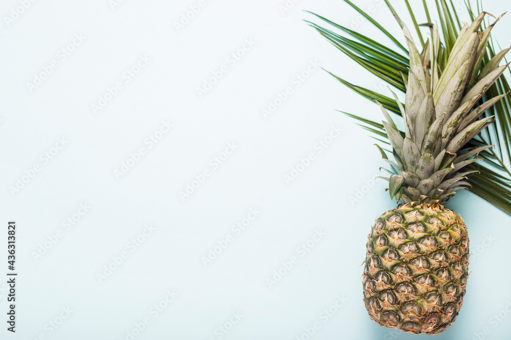 Wall mural whole ripe pineapple and a leaf of a palm tree on a light background. Top view, flat lay